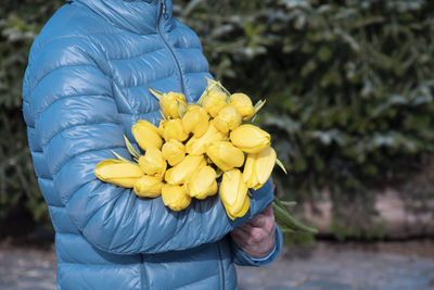 Woman in a blue jacket with a bouquet of yellow spring tulips, mother's day gift