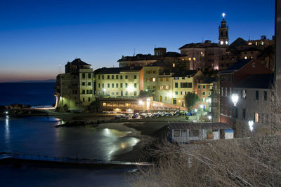 Illuminated buildings by sea against clear sky at night