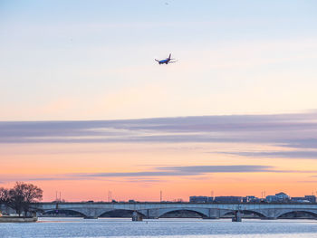 Airplane flying over river against sky during sunset