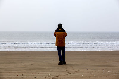 Rear view of man standing at beach against sky