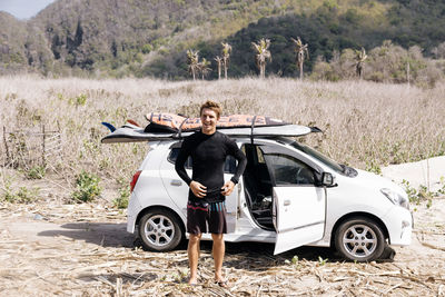 Young man with surfboard near car