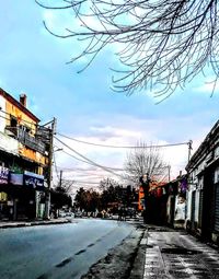 Road by bare trees in city against sky