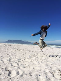 Woman jumping at beach against sky