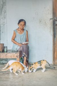 Senior woman looking at cats eating food on floor at home