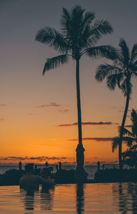 Couple in infinity pool against sky during sunset