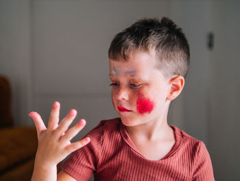 Messy child with brown hair and cosmetic on face in light house on blurred background