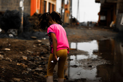 Rear view of girl walking by puddle in city