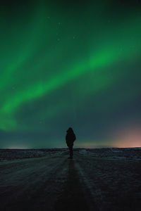 Silhouette man walking on road against sky with northern lights