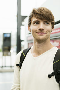 Smiling young man looking away while standing at railroad station