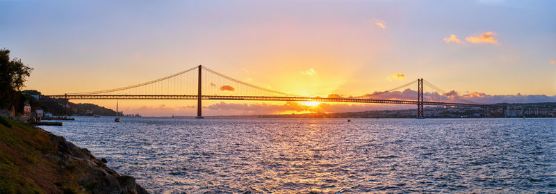 Suspension bridge over river against sky during sunset