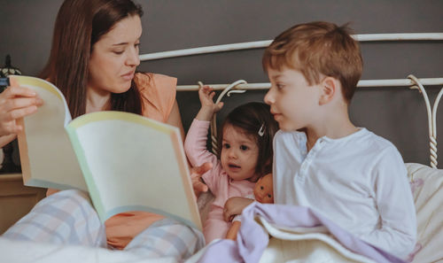 Close-up of mother telling bed time story to children on bed at home