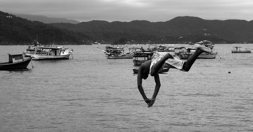 Full length of shirtless man diving into sea by mountains