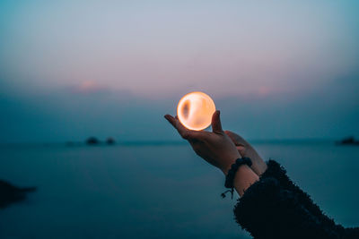 Hand holding sea against sky during sunset