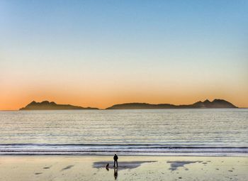 Father and daughter at beach against clear sky during sunset