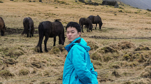 Portrait of man standing against horses grazing on field