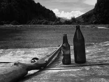 Hunting rifle with beer bottles on wooden plank by field