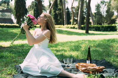 Woman with flowers sitting by wine bottle on picnic blanket