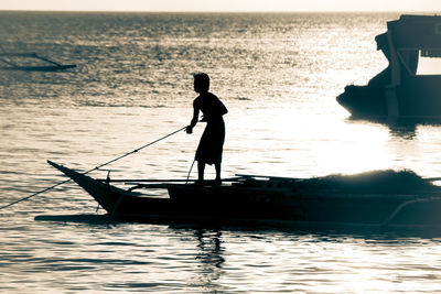 Silhouette man standing on sea against sky during sunset