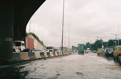 Cars on street by canal against sky in city