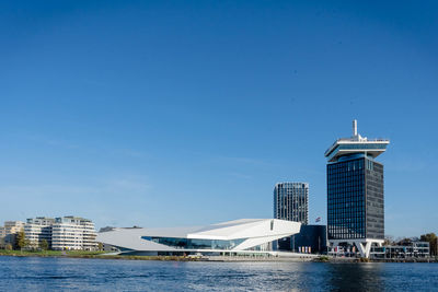 Modern buildings by river against blue sky