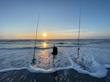 Silhouette fishing rods on beach against sky during sunset while surf fishing