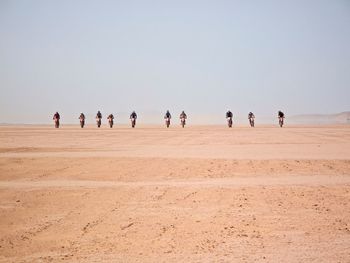 People riding dirt bike at desert against clear sky