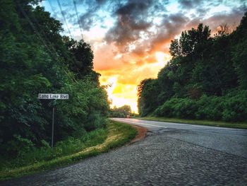 Road passing through forest against cloudy sky