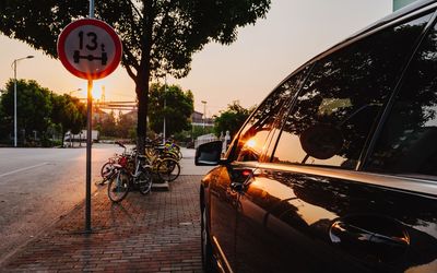 Road sign by trees against sky during sunset