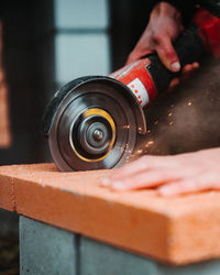 Cropped hands of man cutting brick with equipment