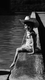 Portrait of girl sitting on retaining wall against lake