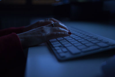 Cropped hands of woman using computer keyboard on table in darkroom at home