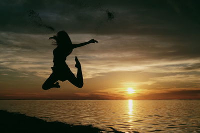 Silhouette man jumping in sea against sky during sunset