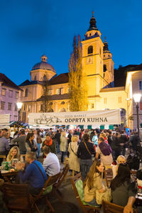 People on street by illuminated buildings in city against sky