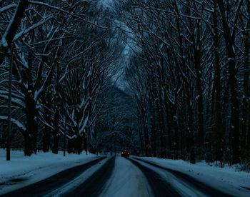 Snow covered road amidst bare trees during winter