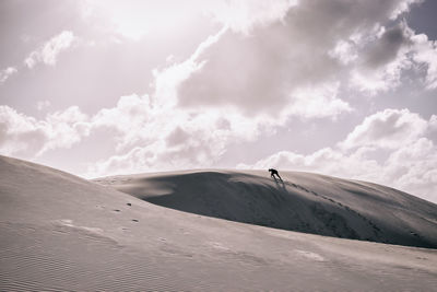 Silhouette person climbing on sand dunes against sky