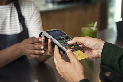 Midsection of female owner taking credit card payment from customer at bar counter in cafeteria