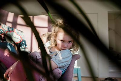 View of a child sitting on a chair at home reading with her brother