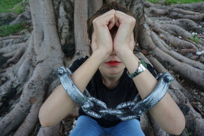 Low section of woman wearing handcuffs while sitting on tree trunk