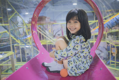 Side view full length portrait of smiling innocent girl sitting in slide