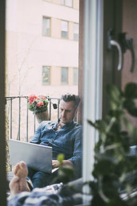 Man resting on balcony working on laptop