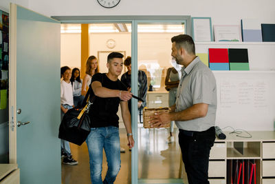 Teenage boy giving phone to professor while walking in classroom