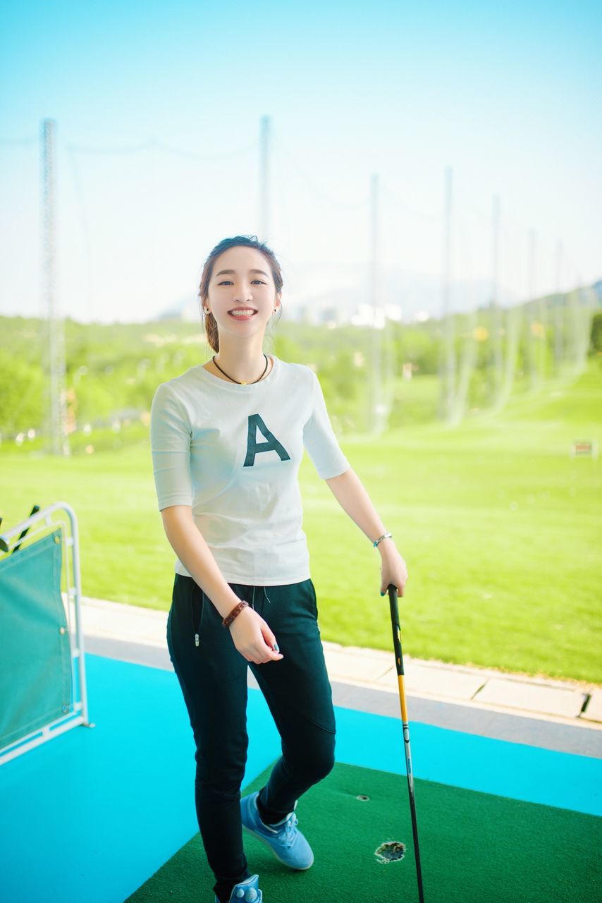 person, grass, leisure activity, lifestyles, casual clothing, childhood, young adult, smiling, portrait, green color, field, full length, looking at camera, happiness, sitting, fun, front view, playground