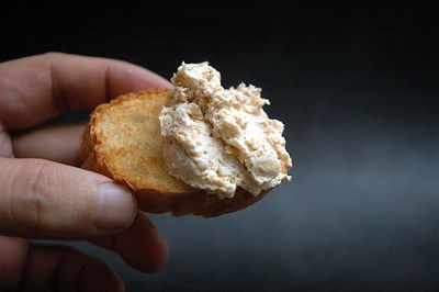 Close-up of hand holding pate on toast against black background