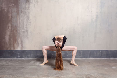 Full length portrait of woman sitting against wall