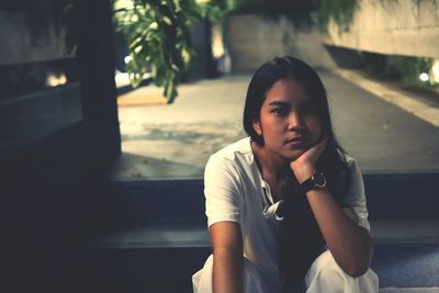 Portrait of young woman with hand on chin sitting on steps at night