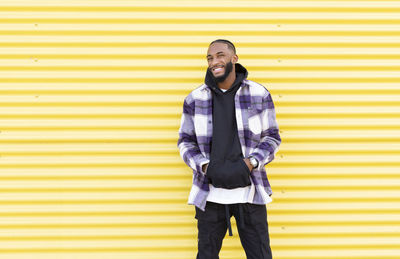 Portrait of young man standing against yellow wall