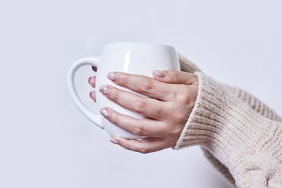 Female hand holding hot tea cup against white background. a woman in warm knitted sweater holds in