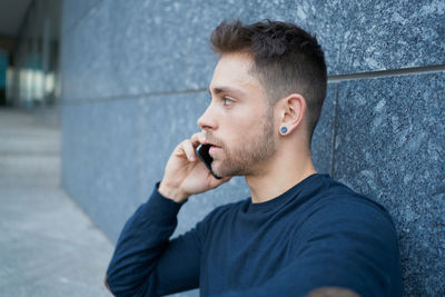 Side view of modern male in casual wear sitting near stone wall and br