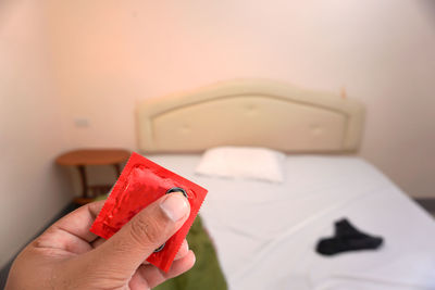 Cropped hand holding condom packet in bedroom