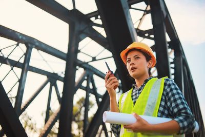 Beautiful asian engineer woman in hard hat holding walking around at construction site.